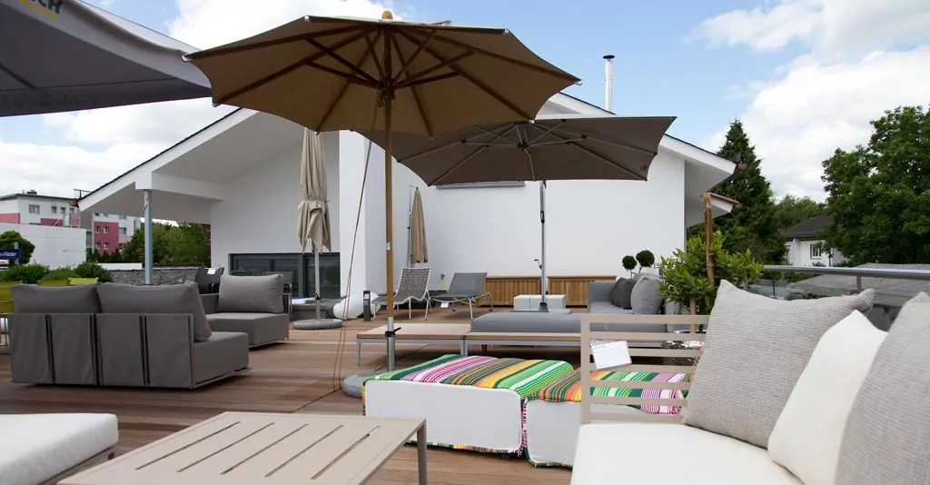 Abendliche Terrasse mit beleuchtetem rotem Sonnenschirm Sitzbereich in grau und beige mit passenden Kissen