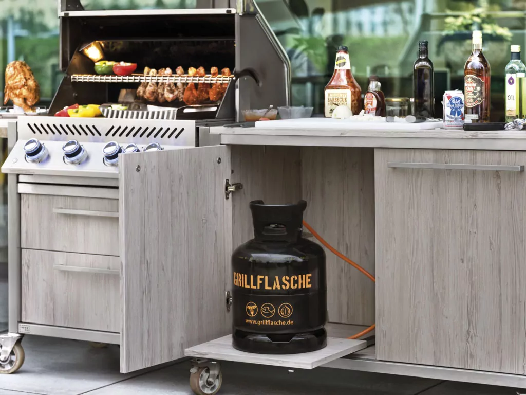 Abendliche Terrasse mit beleuchtetem rotem Sonnenschirm Outdoor Küche in Holzoptik mit Grill