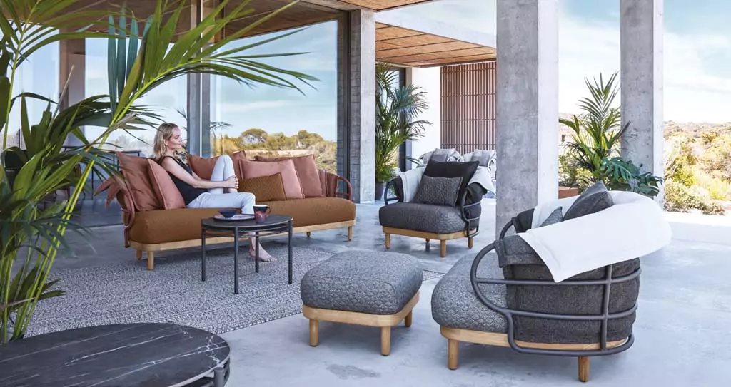 Abendliche Terrasse mit beleuchtetem rotem Sonnenschirm Outdoor Sitzbereich mit braunem Sofa und grauen Sesseln