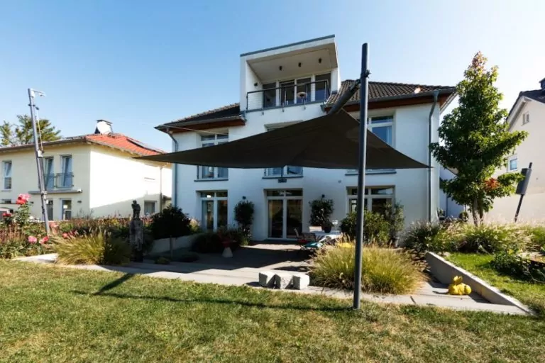 Automatische Terrassenbeschattung mit Fernbedienung Schwarzes Sonnensegel vor weißem Haus